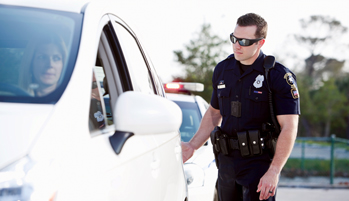 A uniformed police officer approaches a stopped car. 