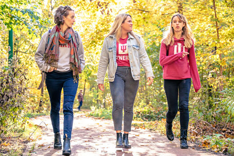 Three female students in O'Neill shirts walk on a wooded path